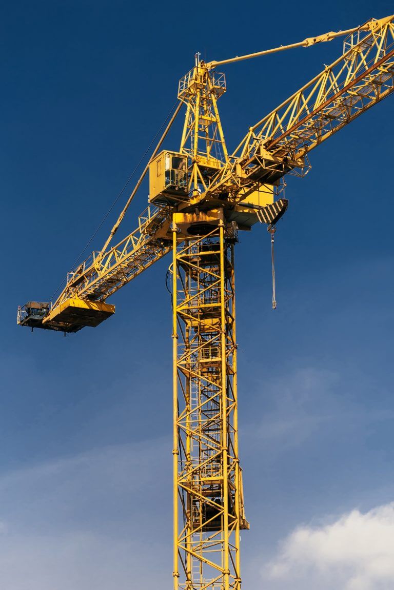 Construction crane tower in sun light beams on background of blue sky
